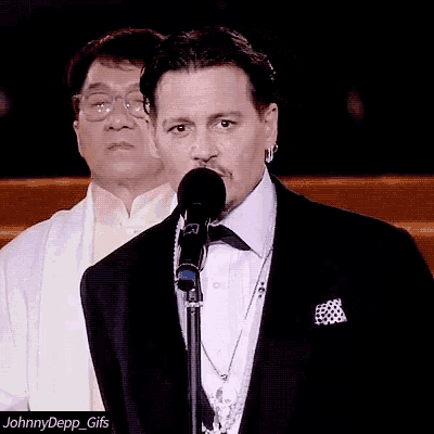 a man in a tuxedo stands in front of a microphone with the caption johnnydepp_gifs below him