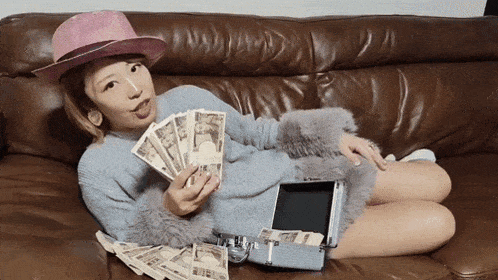 a woman is laying on a couch holding a fan of money