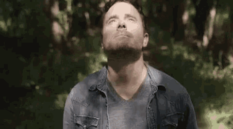 a man is sitting in the woods with his eyes closed .