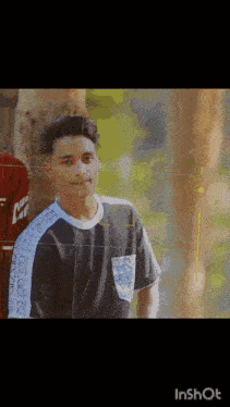 a boy wearing a shirt that says ' nk ' on it is standing next to a tree