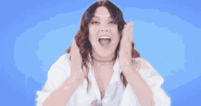 a woman in a white shirt is making a funny face with her mouth open and her hands in the air .
