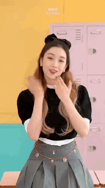 a woman in a black top and gray skirt is standing in front of a pink locker .