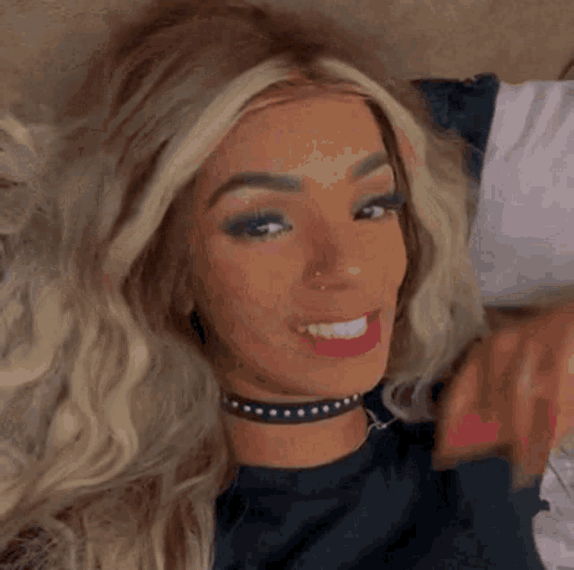 a blonde woman wearing a choker and red lipstick smiles