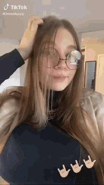 a woman wearing glasses and a black turtleneck is making a hand gesture .