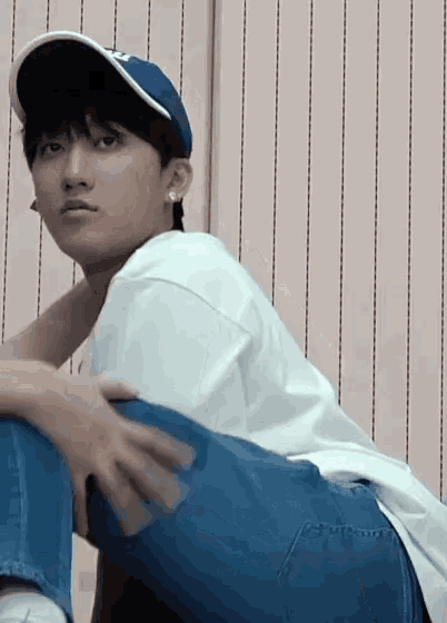 a young man wearing a baseball cap and jeans is sitting on the floor
