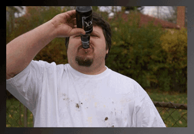 a man in a white shirt is drinking from a dirty bottle that says ' x ' on it