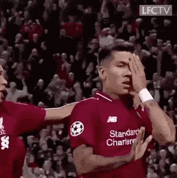 a soccer player is covering his eyes with his hands while another player hugs him .