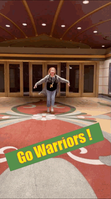 a woman is jumping in front of a building with a sign that says go warriors