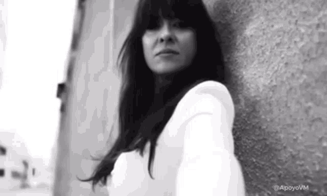 a black and white photo of a woman standing next to a wall .