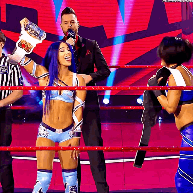 a woman in a wrestling ring holds up a championship belt while a man in a suit stands behind her