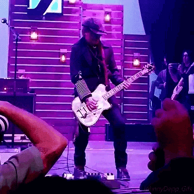 a man playing a guitar on a stage with a purple background behind him