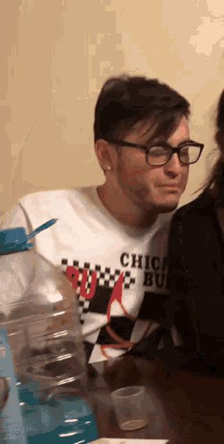 a man wearing glasses and a shirt that says chica bull is sitting at a table