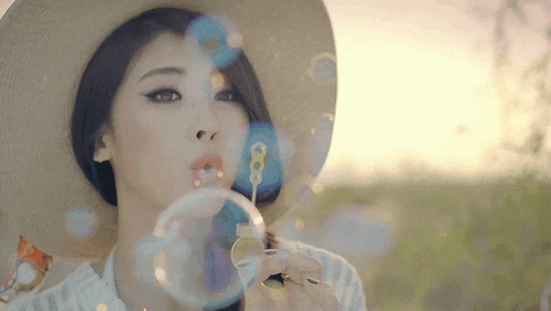 a woman wearing a hat blowing soap bubbles in a field
