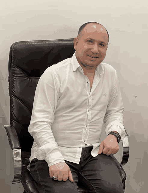 a bald man in a white shirt is sitting in a leather chair