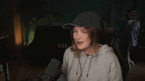 a woman wearing a hat and a hoodie is giving the middle finger in front of a microphone