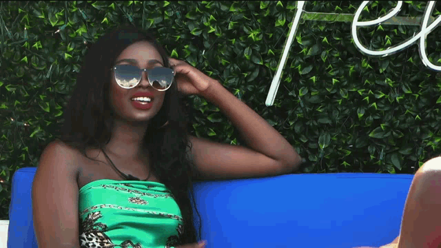 a woman wearing sunglasses and a green top is sitting on a blue couch