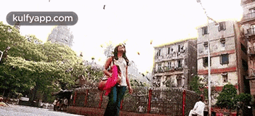 a woman walking down a street with birds flying around her and the words kulfyapp.com on the bottom right