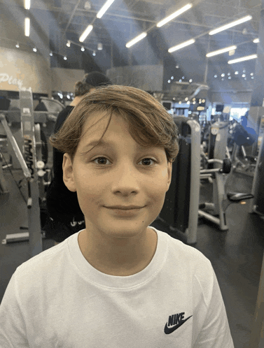 a young boy wearing a white nike t-shirt smiles in a gym