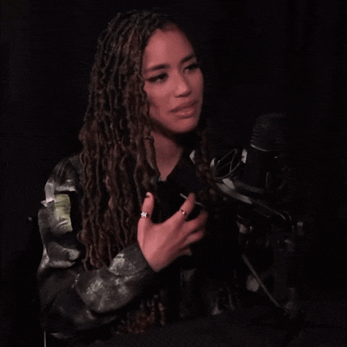 a woman with dreadlocks is speaking into a microphone in a dark room