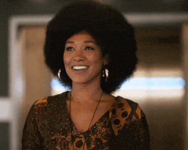 a woman with a large afro is smiling and wearing earrings