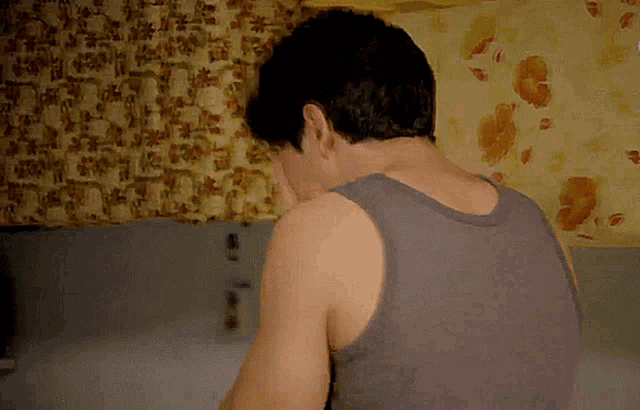 a man in a gray tank top wipes his face