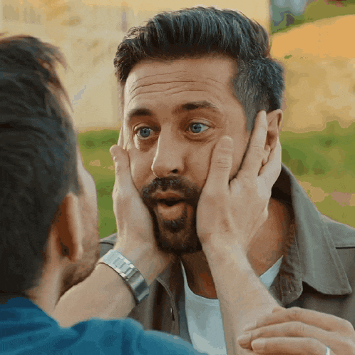 a man with a watch on his wrist is touching another man 's face with his hands
