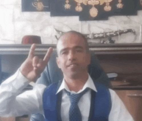 a man wearing a blue vest and tie is giving the peace sign