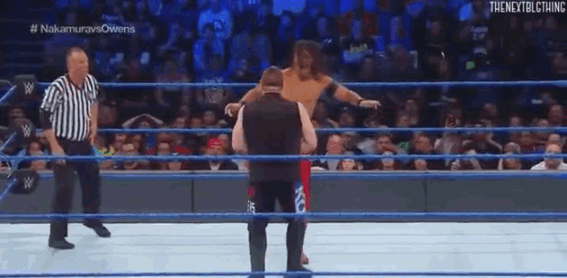 a wrestler is standing in a wrestling ring with a referee watching .