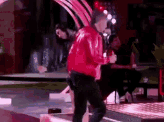 a man in a red jacket is dancing on a stage with a microphone .