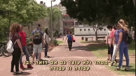 a group of people standing on a brick sidewalk with hebrew writing on the bottom of the screen