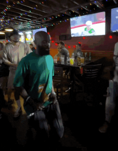 a man in a green shirt is standing in a crowded bar