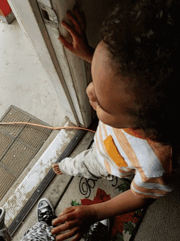 a young boy reaches for a door handle while sitting on a door mat