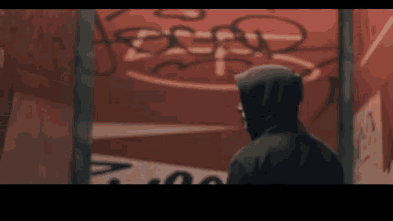 a person in a hoodie stands in front of a wall with graffiti on it that says bear