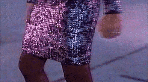 a woman in a pink and blue sequined dress is walking down the street .