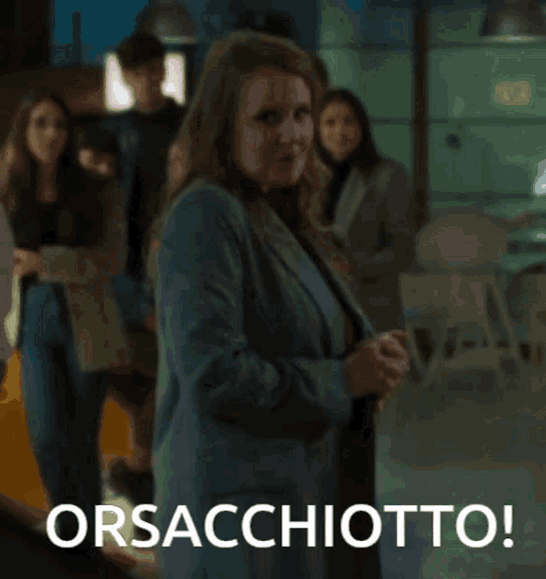 a woman in a suit stands in front of a group of people with the words orsacchiotto written below her