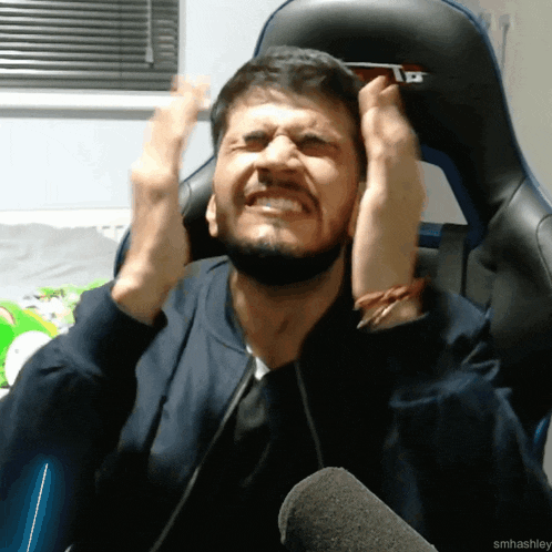 a man with a beard is sitting in a chair with his hands on his head