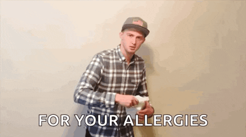 a man in a plaid shirt is blowing his nose while holding a box of toilet paper .
