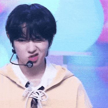 a boy wearing a yellow hoodie and a microphone making a funny face