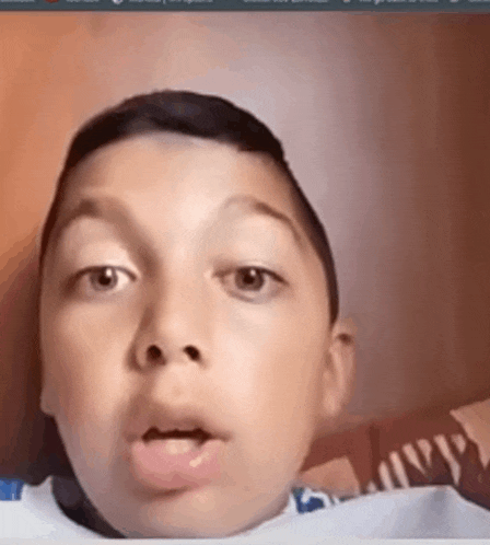 a young boy is making a funny face while sitting on a bed .