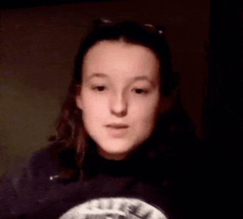 a young girl is giving a thumbs up sign while wearing a black sweatshirt .