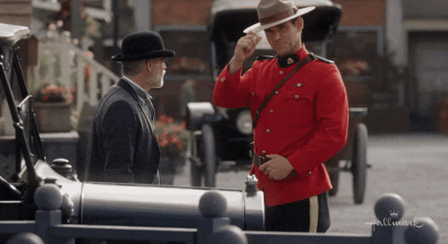 a man in a red uniform is standing next to a man in a bowler hat in front of a hallmark sign