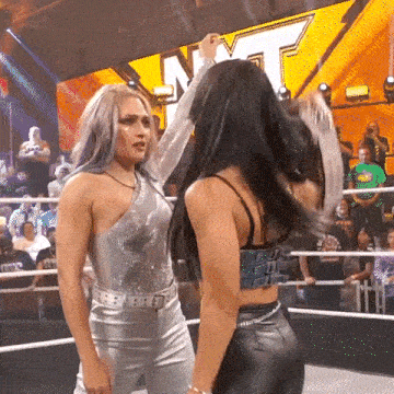 two women are standing in a wrestling ring .