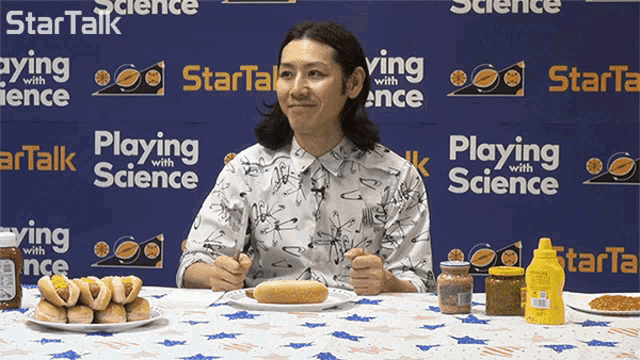 a man eating a hot dog in front of a blue wall that says " playing with science "