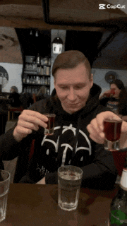a man sitting at a table holding a shot glass and a glass of water