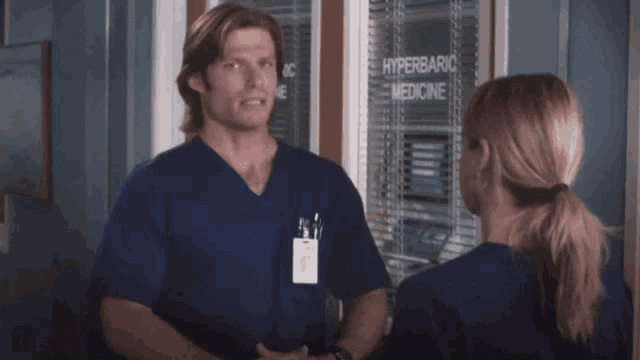 a man and a woman are standing in front of a window that says hyperbaric medicine .