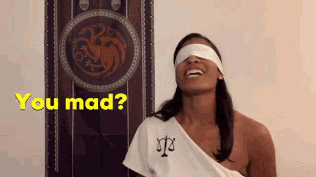 a woman with blindfolds on her eyes is standing in front of a wall with a dragon on it and says `` you mad '' .