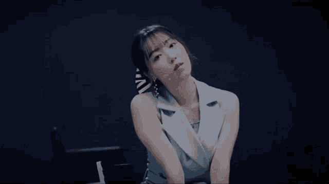 a woman in a blue vest is sitting in a chair in a dark room .