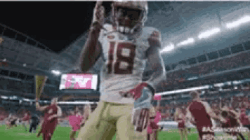 a football player with the number 18 on his jersey is holding a football .