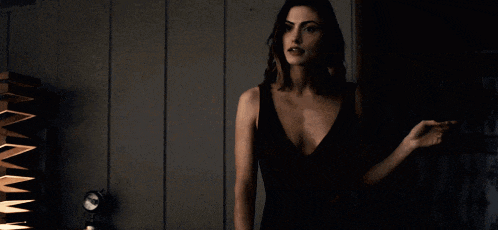 a woman in a black dress with a plunging neckline stands in a dark room