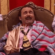a man in a suit and tie is sitting in a chair wrapped in a striped blanket .